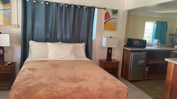 A hotel room with a bed, two bedside tables, a desk with a microwave, and a small kitchenette.