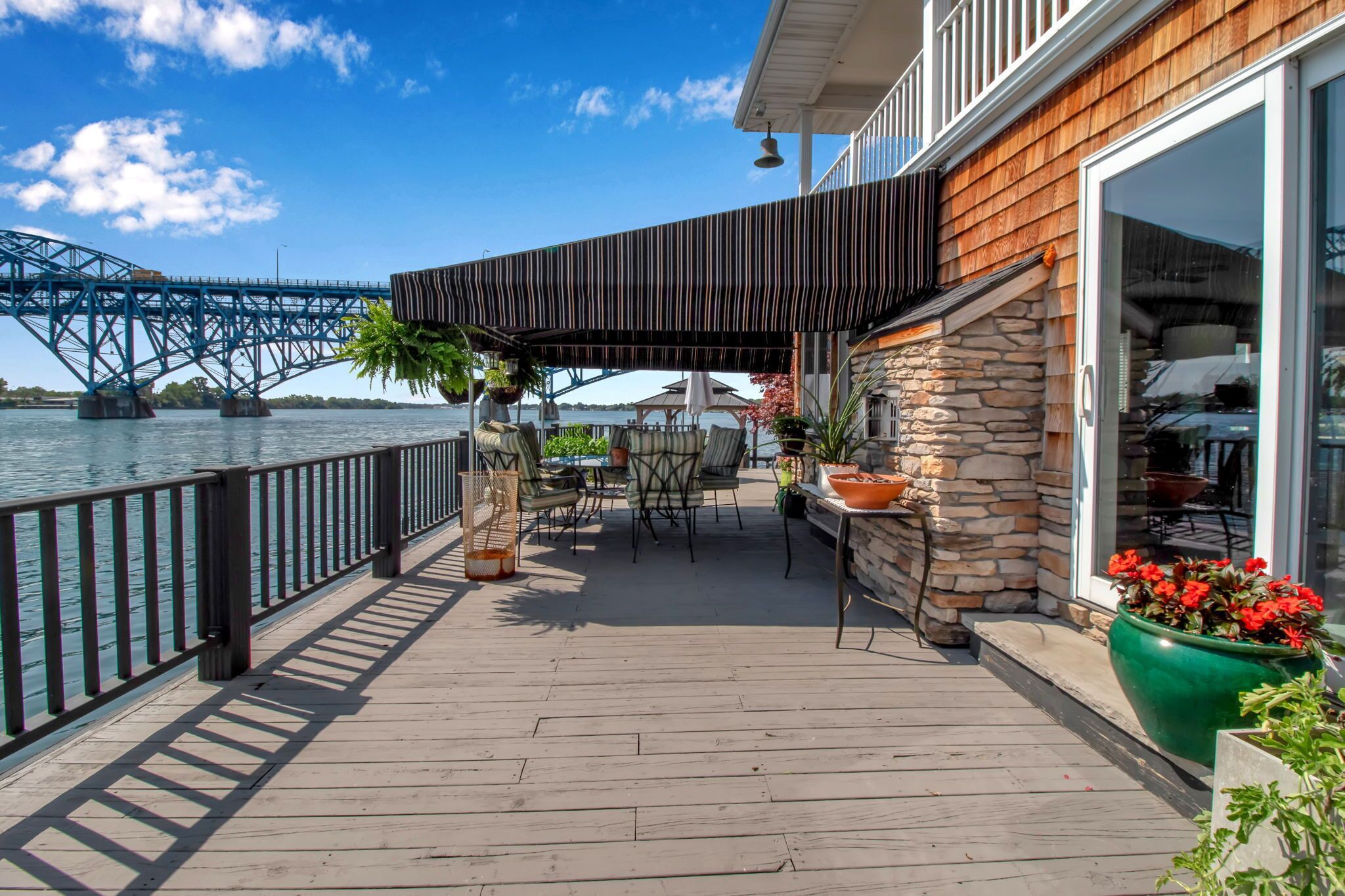 A wooden deck with outdoor furniture, a stone wall, and a view of a bridge over water.