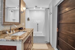 Un baño con lavamanos de mármol, un espejo grande, una bañera y una puerta de madera.