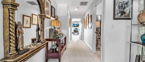 A hallway with a large mirror, framed artwork, and a console table with decorative items.