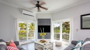 A modern living room with grey sofas, a white coffee table with flowers, a ceiling fan, and a TV on a grey cabinet. - Newly Updated Beach House @ Famous French Leave Bch, Htd Pool, Paddle Boards (Governors Harbour)