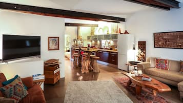 Un salon moderne avec un canapé, une table basse et un téléviseur. Au fond, on aperçoit une cuisine avec un coin repas.