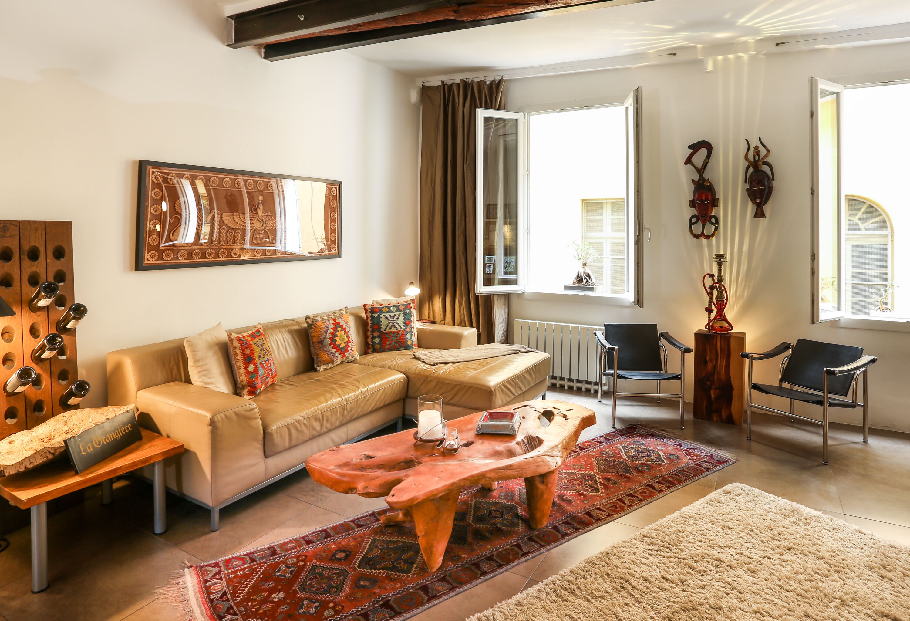 Un salon avec un canapé, une table basse et des fauteuils. Il y a une fenêtre avec des rideaux, un radiateur et des œuvres d’art accrochées au mur.