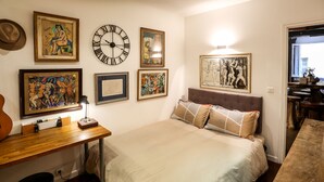 Een slaapkamer met een bed, een houten bureau en diverse ingelijste kunstwerken aan de muur.