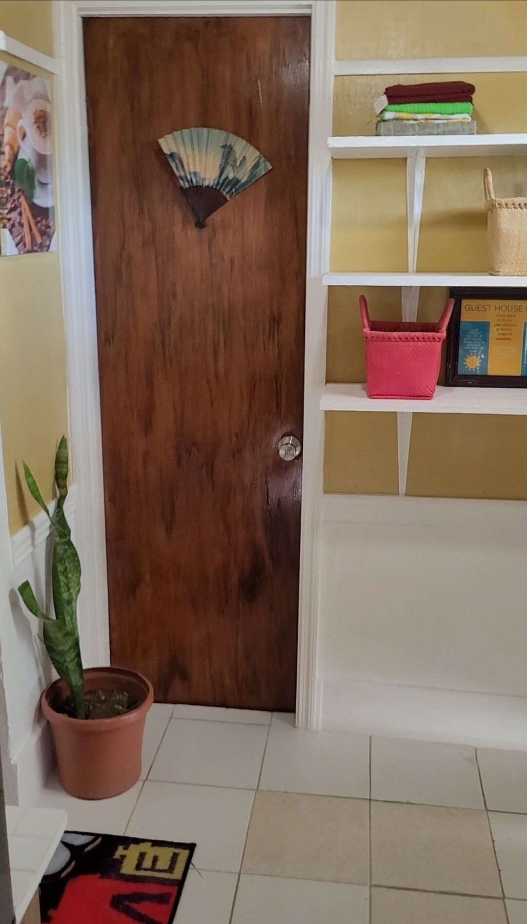 Une porte en bois ornée d’un motif en éventail, un pot de fleurs et un panier rouge posés sur une étagère.