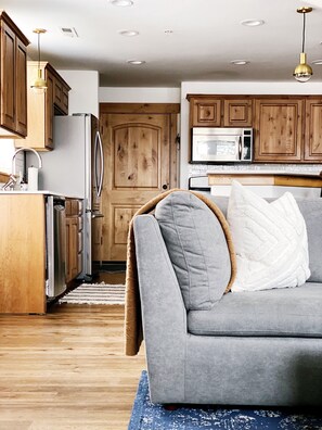 A modern kitchen with wooden cabinets, a grey sofa, and a blue rug.