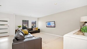 Ein modernes Wohnzimmer mit einem grauen Sofa, einem kleinen Tisch mit Lampe und einem gerahmten Bild an der Wand.