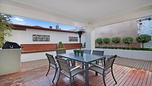 Eine überdachte Terrasse mit Glastisch und -stühlen, einem Grill und dekorativen Wandbildern.