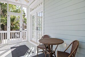Un porche cubierto con una mesa y sillas de mimbre, una puerta blanca y vistas de follaje exterior.