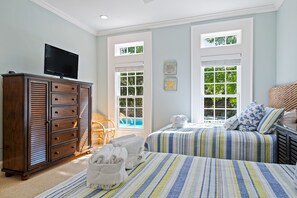 Un dormitorio con dos camas, un aparador, un televisor y una ventana con vista a árboles.