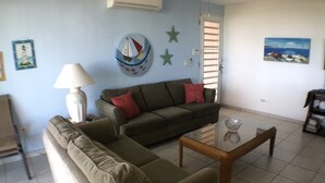 A living room with a sofa, a coffee table, and a lamp. There are wall decorations including a sailboat and stars. - OCEAN VIEW "GATED" AND ACROSS THE WYNDHAM HOTEL!!! (RIO GRANDE RIO MAR)