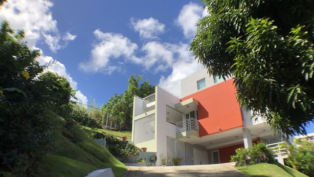 A modern two-story building with a red facade and white accents, surrounded by lush greenery and a clear blue sky. - OCEAN VIEW "GATED" AND ACROSS THE WYNDHAM HOTEL!!! (RIO GRANDE RIO MAR)