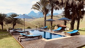 Un área de piscina con terraza de madera, sillas de descanso y sombrillas.