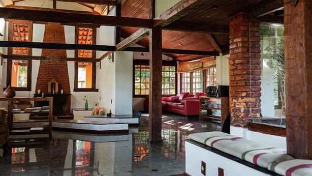 Una habitación amplia con techo alto, vigas de madera, chimenea de ladrillo y sofá rojo.