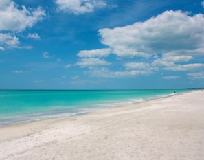 Une vaste plage de sable fin, bordée d’une eau turquoise et limpide, et surplombée d’un ciel dégagé.