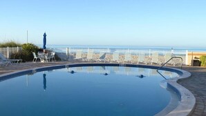 A swimming pool with a view of the ocean, surrounded by lounge chairs and umbrellas. - Beachcomber unit 201 (Longboat Key)