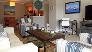 A living room with a sofa, armchairs, a coffee table, a TV, and a painting of a sailboat. - Beachcomber unit 201 (Longboat Key)