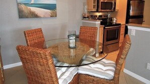 A dining area with wicker chairs, a glass table, and a painting of a sailboat on the wall. - Beachcomber unit 201 (Longboat Key)