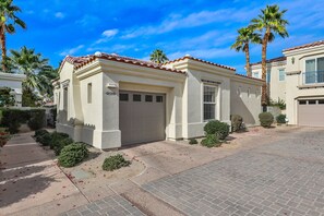 A residential building with a garage, palm trees, and a clear blue sky.