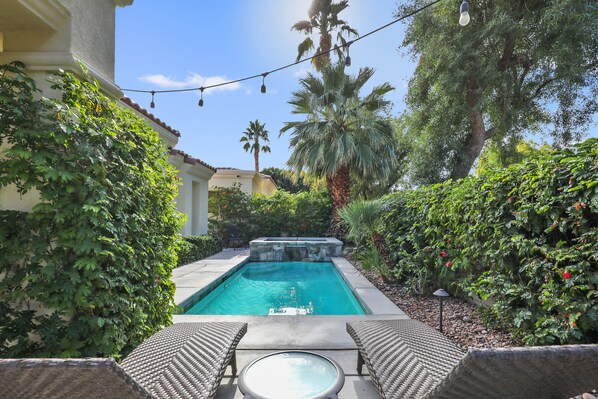 A swimming pool with lounge chairs and a hot tub, surrounded by greenery and palm trees.
