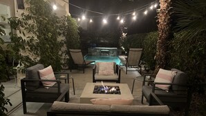Un patio exterior con piscina, rodeado de sillas y un pozo de fuego.