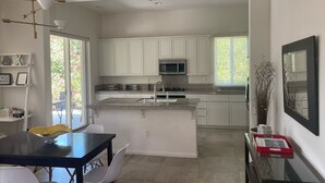 Una cocina moderna con armarios blancos, una isla central y una zona de comedor con una mesa negra y sillas blancas.