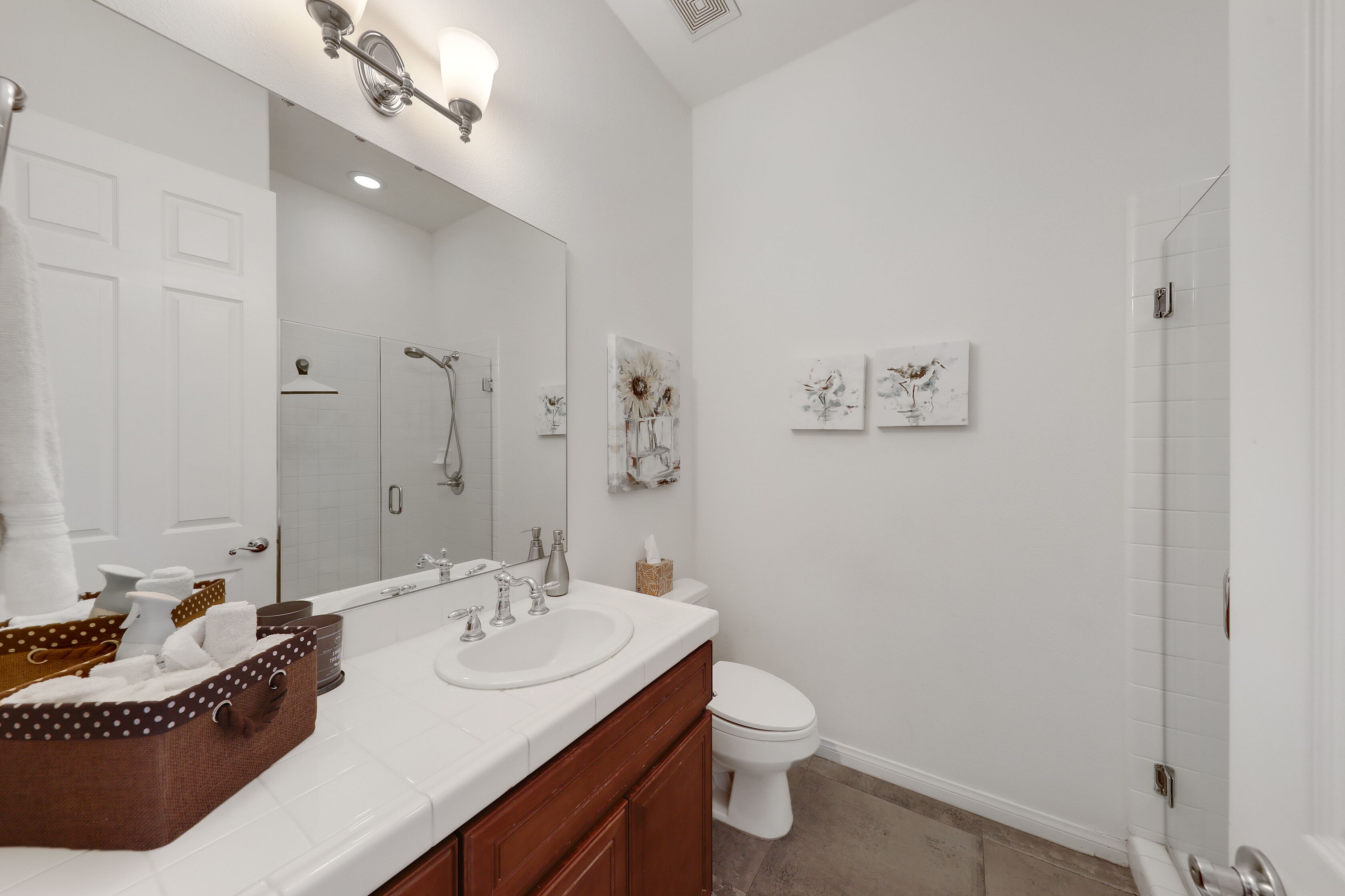A bathroom with a white sink, vanity, and toilet. There is a shower area with a glass door and a towel rack with towels.