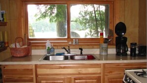 A kitchen with wooden cabinets, a stainless steel sink, a stove, and a window with a view of trees.