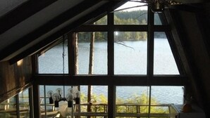 A room with large windows overlooking a lake, a ceiling fan, and a wooden deck outside.