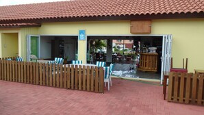 Een terras met houten stoelen en tafels, een houten hek en een gebouw met een pannendak.