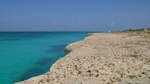 Een rotsachtig strand met helder turquoise water en boten in de verte.
