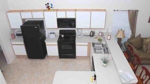 Une cuisine compacte équipée d’un réfrigérateur, d’un four à micro-ondes et d’une cuisinière. Elle comprend également un coin repas avec une table et des chaises.