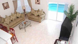 Un salon avec deux canapés, une table basse et un téléviseur. Une porte-fenêtre coulissante donne accès à une piscine.