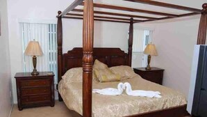 Un lit à baldaquin avec une structure en bois, deux tables de chevet avec des lampes et une couvre-lit ornée de deux cygnes blancs.