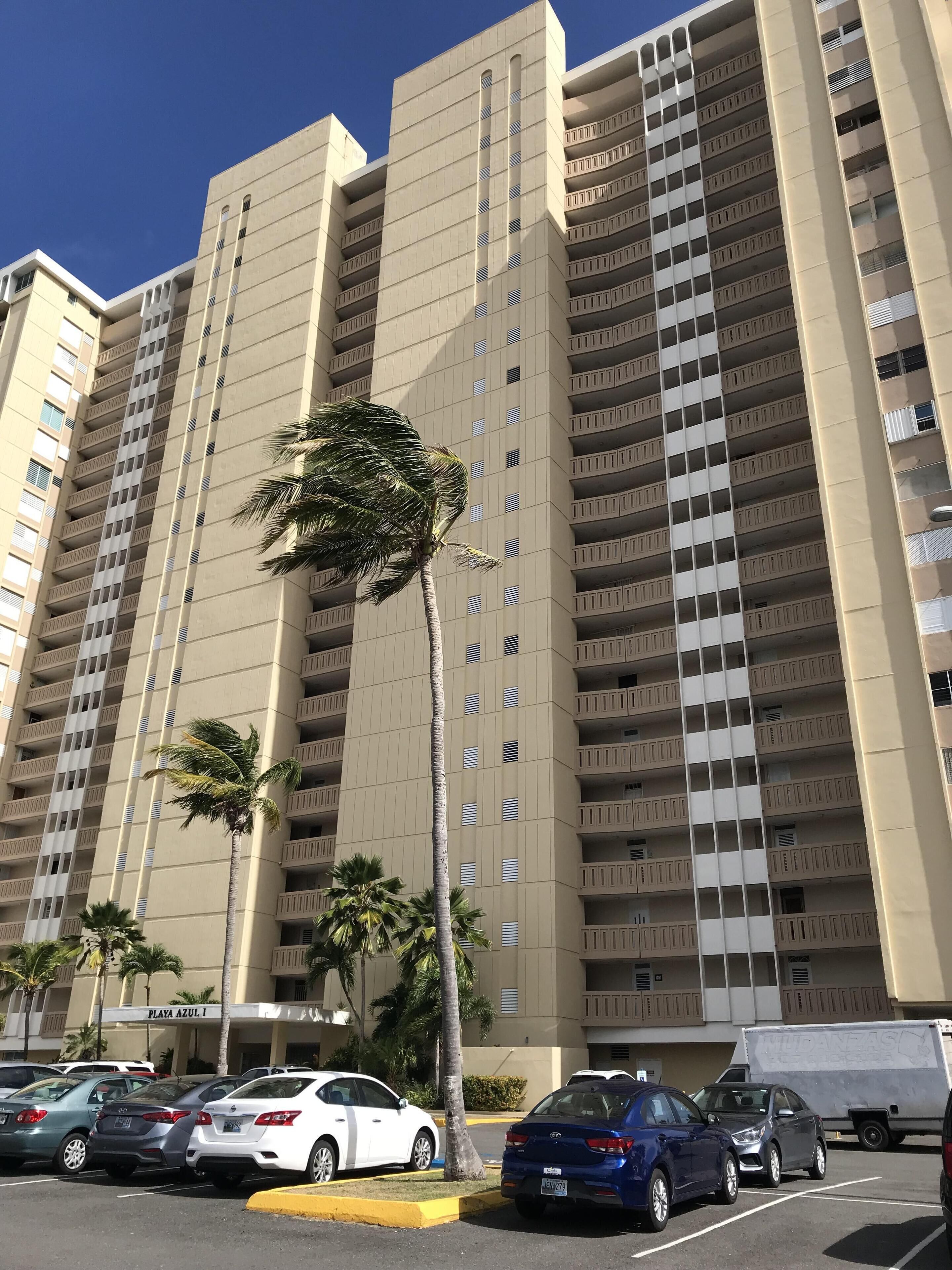 A high-rise building with multiple balconies and a parking lot in front.