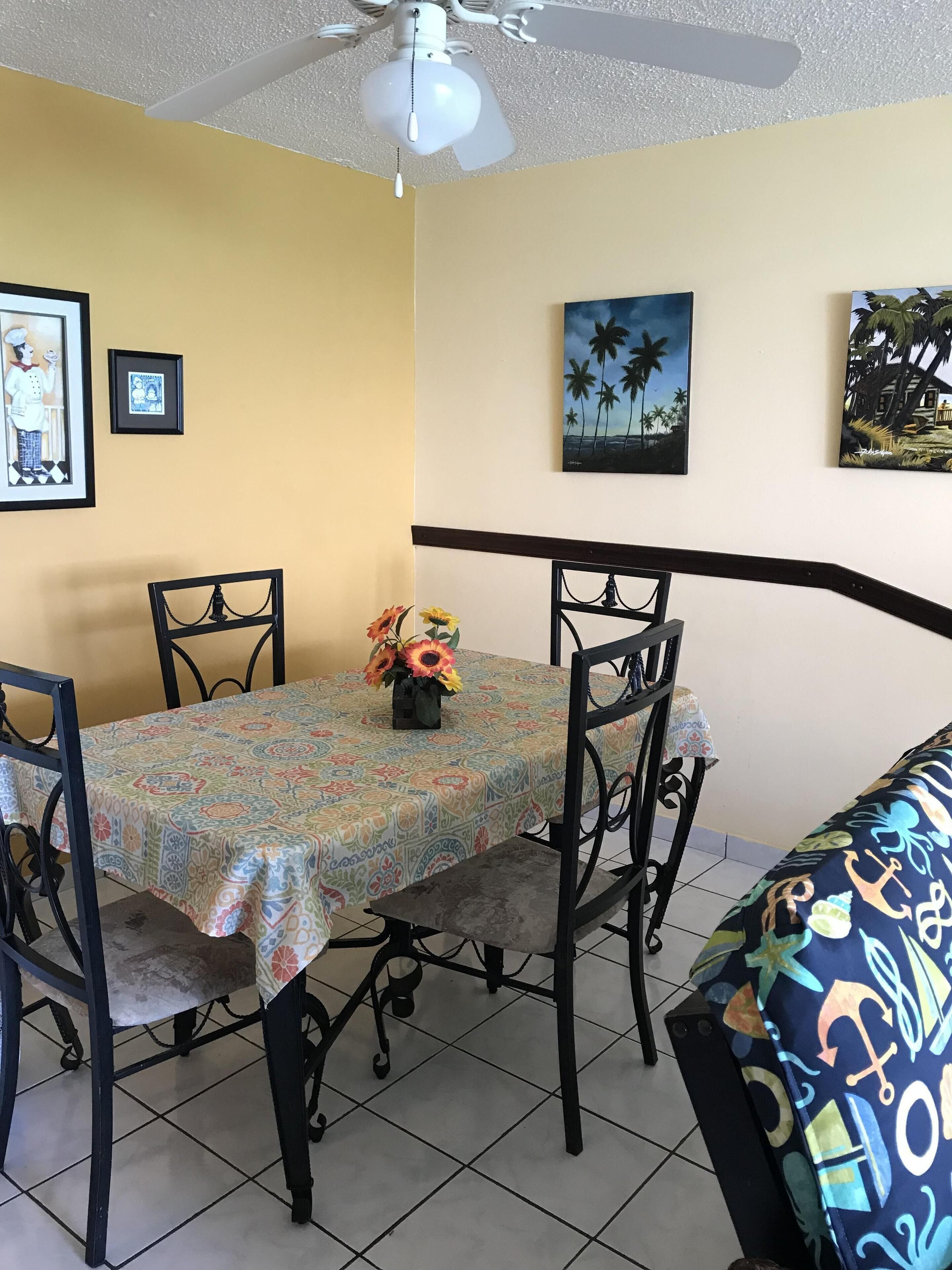 A dining area with a table covered by a patterned tablecloth, surrounded by chairs.