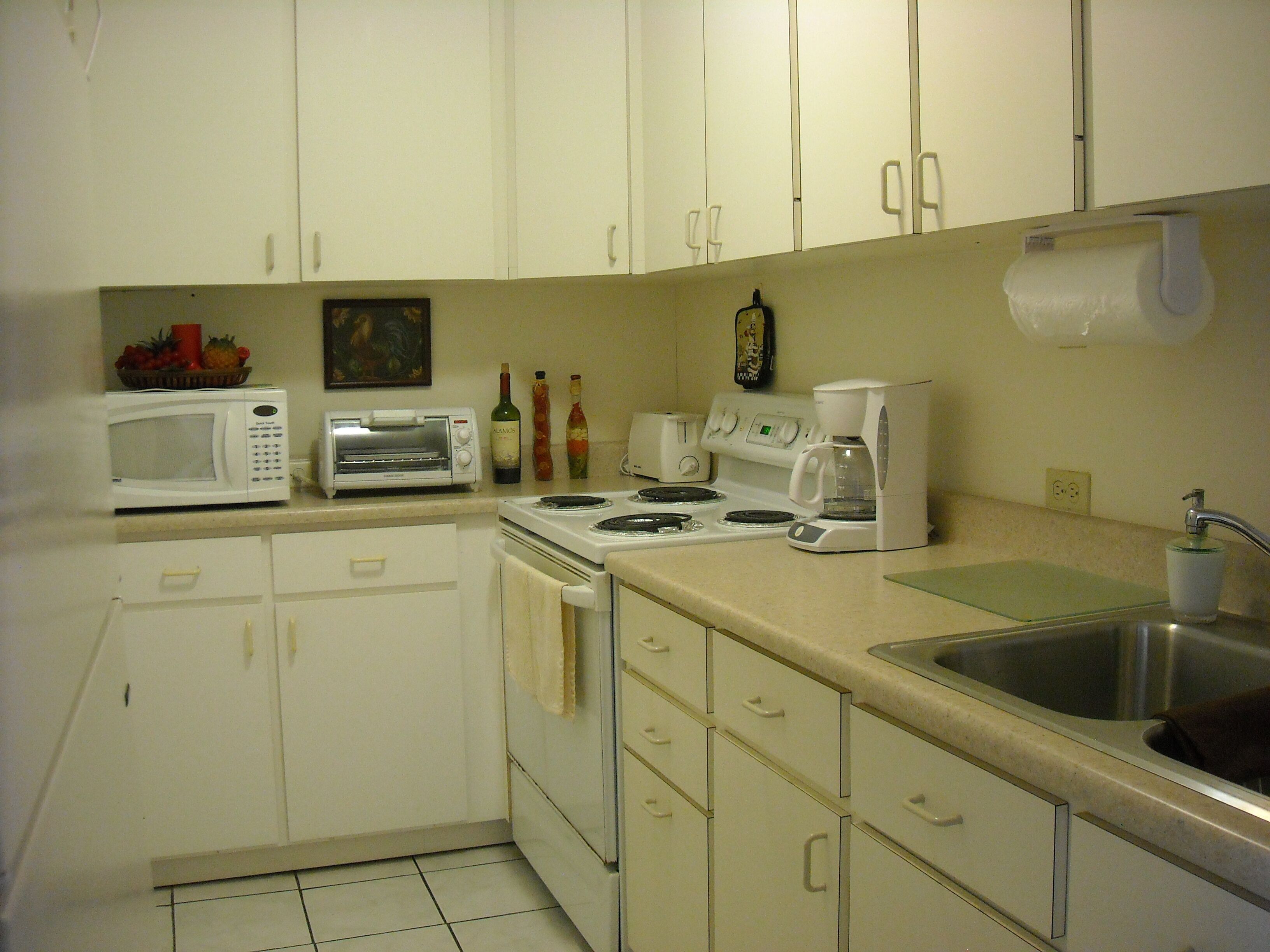A kitchen with white cabinets, a microwave, a toaster, a stove, and a coffee maker.