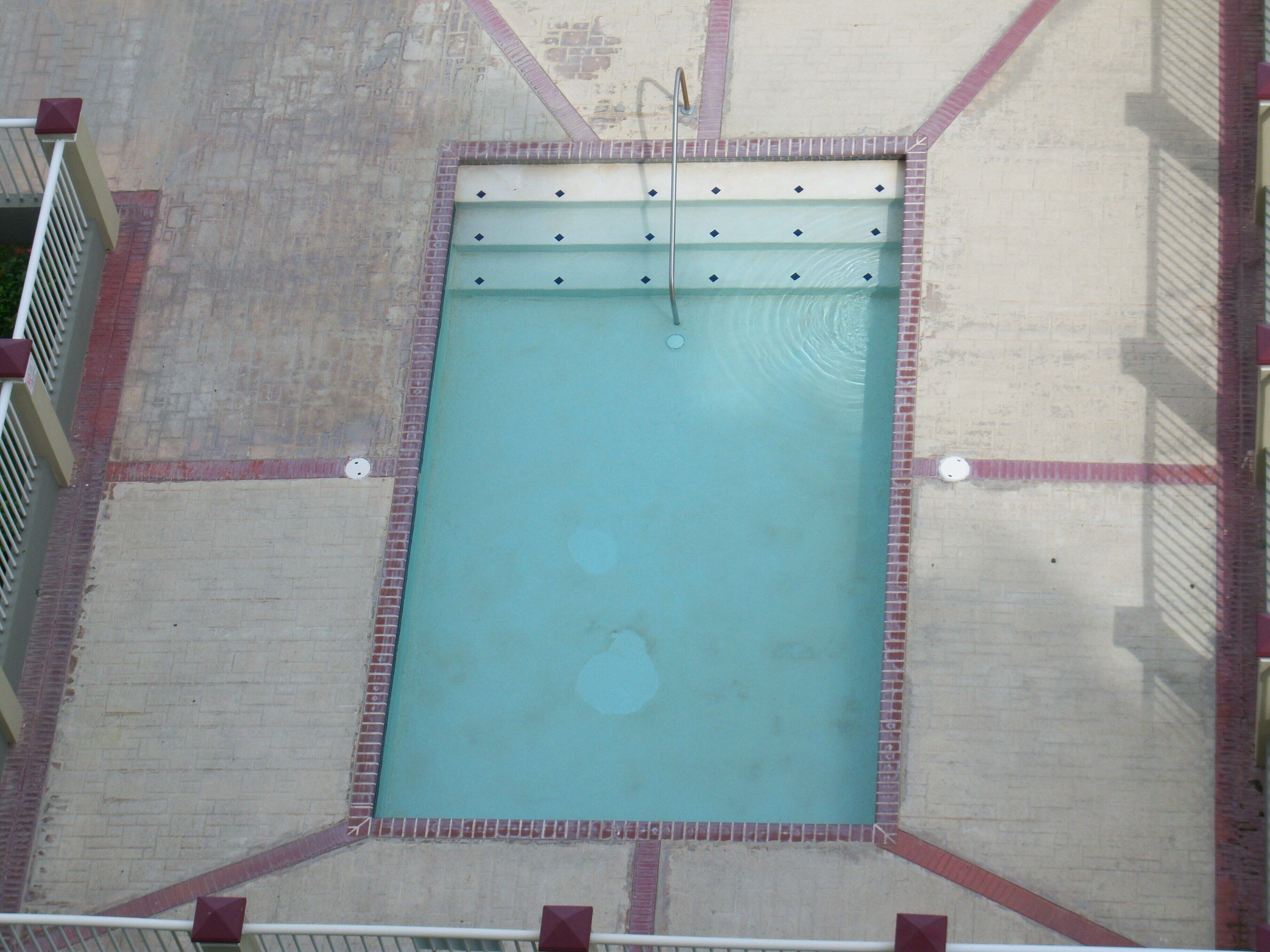 Vue aérienne d’une piscine rectangulaire bordée de carreaux et dotée d’un escalier en métal.