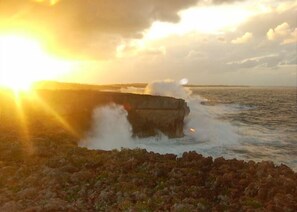 A rocky coastline with waves crashing against a large rock formation during sunset. - Private Beachfront Estate w/Heated Pool on Pink Sand Beach (Double Bay)