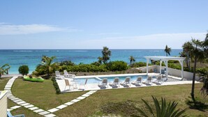 Un espace piscine doté de chaises longues et d’un cabanon offrant une vue sur l’océan.