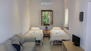 A small, clean room with two single beds, a sofa, a TV, and a window with a view of greenery. - 'Perivoli' Stone House (Eresos Lesbos)