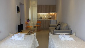 A compact hotel room with two beds, a small kitchenette, a sofa, and a TV. - 'Perivoli' Stone House (Eresos Lesbos)