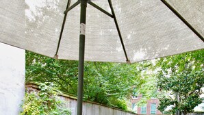 An outdoor patio with a table set for dining, surrounded by chairs and a large umbrella.
