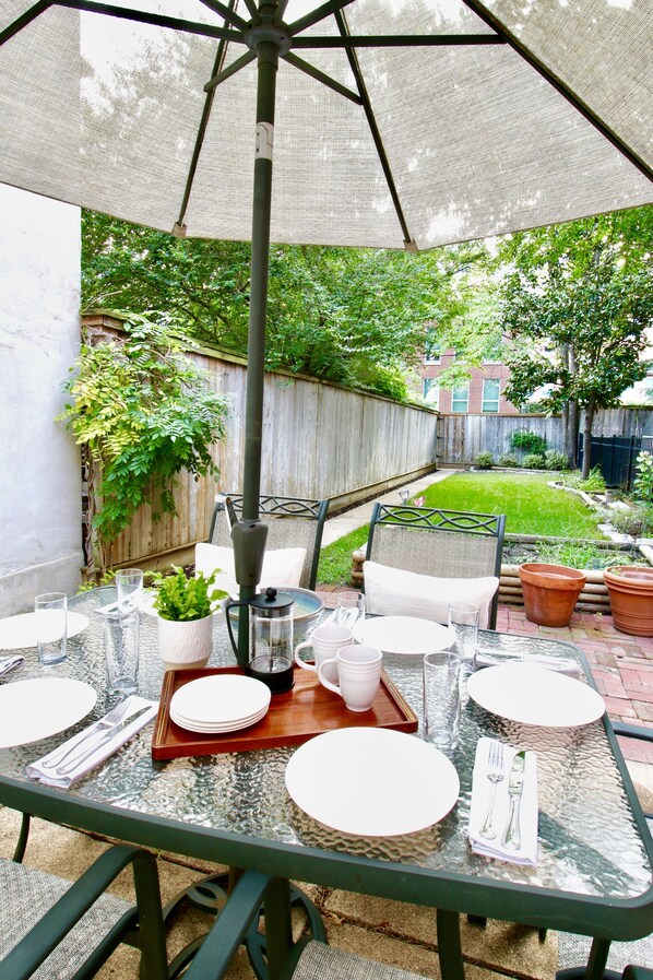 An outdoor patio with a table set for dining, surrounded by chairs and a large umbrella.