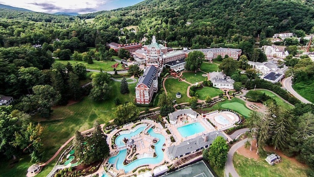 Vista aérea de un complejo turístico con una piscina grande, varias construcciones y abundante vegetación.