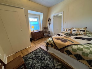 A bedroom with a bed, a dresser, a chair, a window with blinds, and a door.