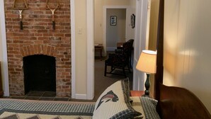 Una habitación con chimenea de ladrillo, una cama con colcha, una lámpara y una silla.