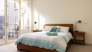 A bedroom with a large bed, a nightstand, a desk, and a chair. - One Level at Broadbeach - Inverloch (Inverloch)