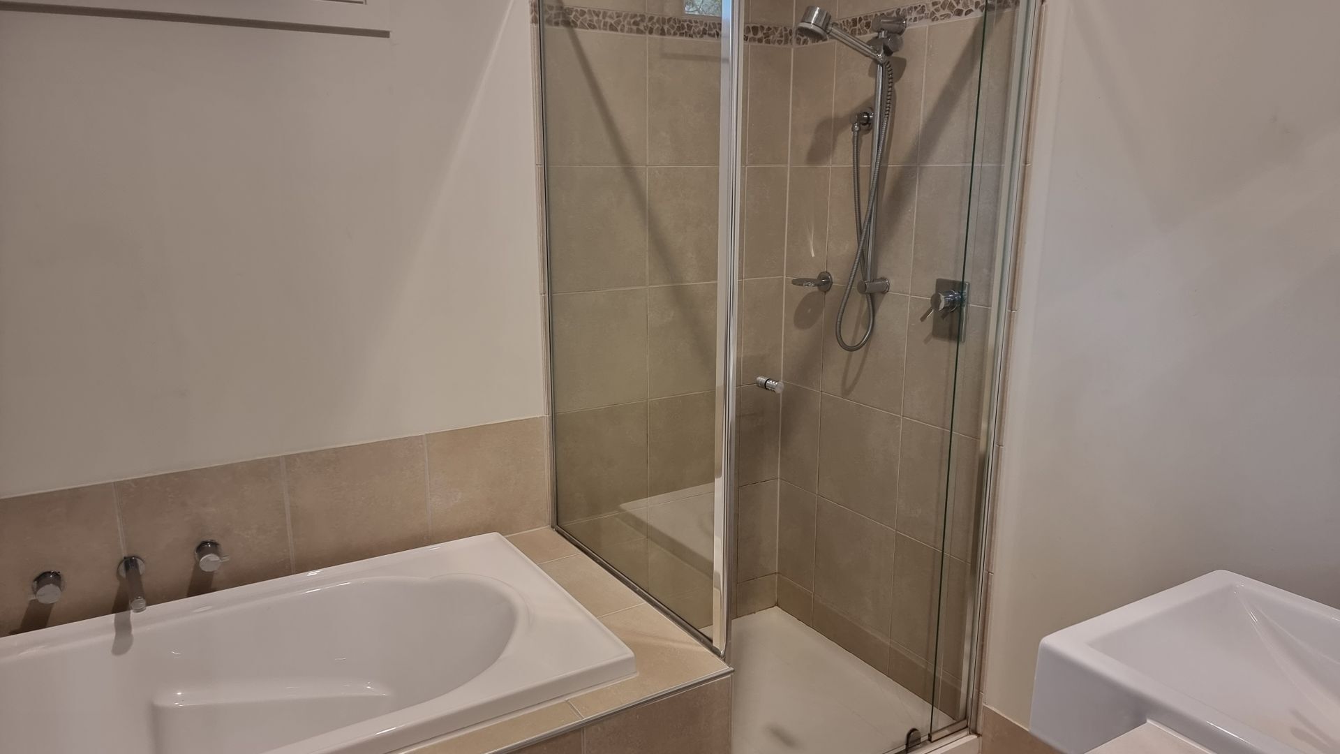 Une salle de bain avec une douche à parois de verre, une baignoire blanche et un lavabo blanc.