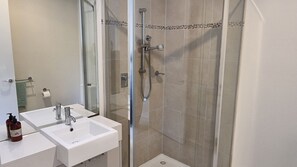 Une salle de bain avec deux lavabos blancs, une douche en verre et un sol carrelé.